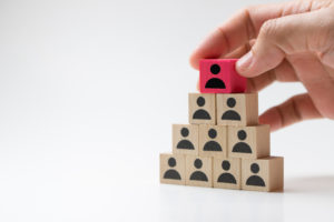 Hand putting wood cube block on top pyramid for leadership concept